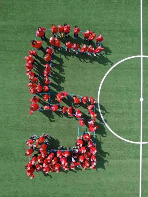 Students in red forming the number 5 on the football pitch