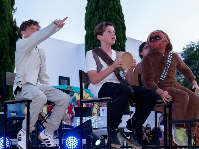 Secondary students performing a drama sketch on stage, one dressed as a Wookiee
