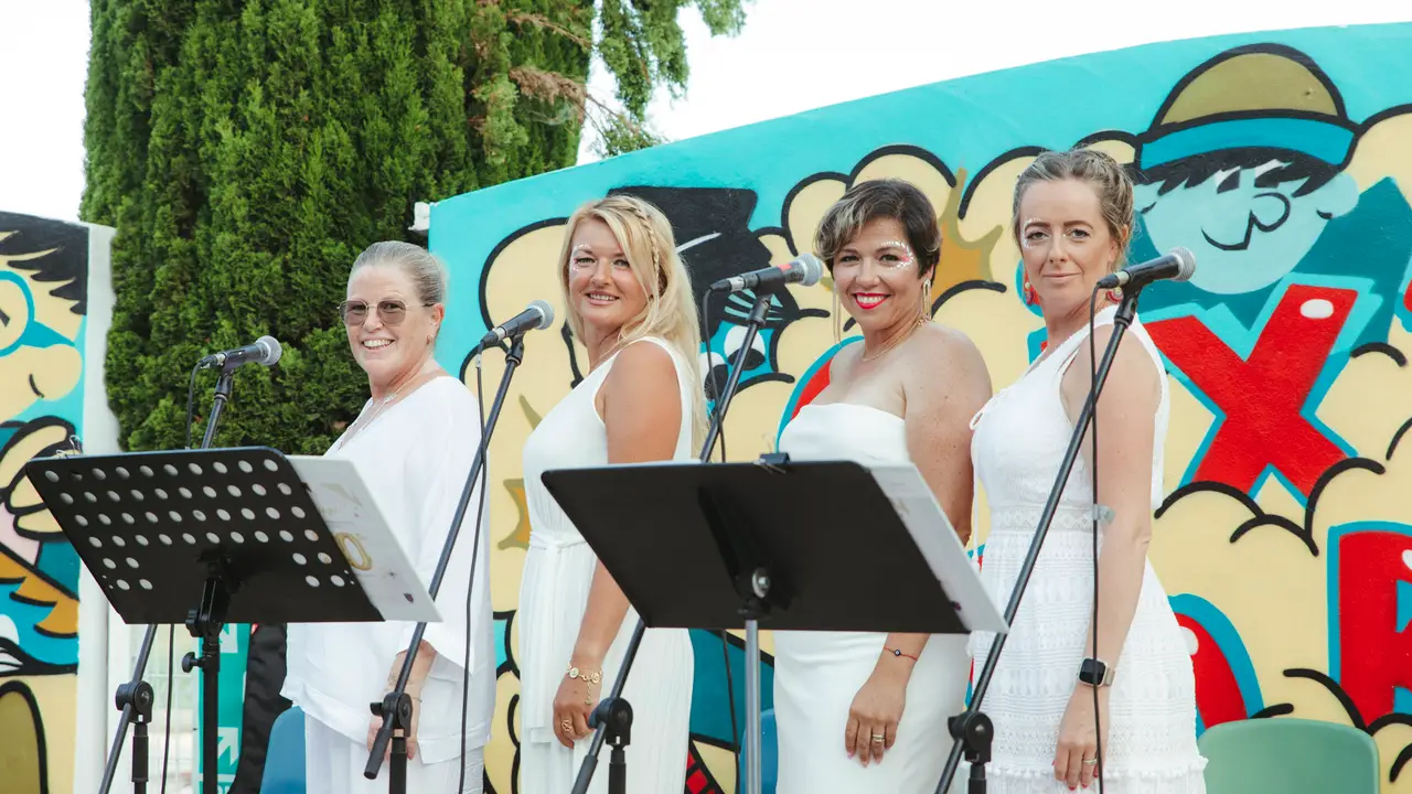 Four singers dressed in white performing in front of a colourful graffiti wall at Morna's 50th Anniversary celebration
