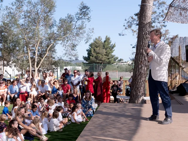 A speaker addressing the crowd gathered on the lawn under the trees