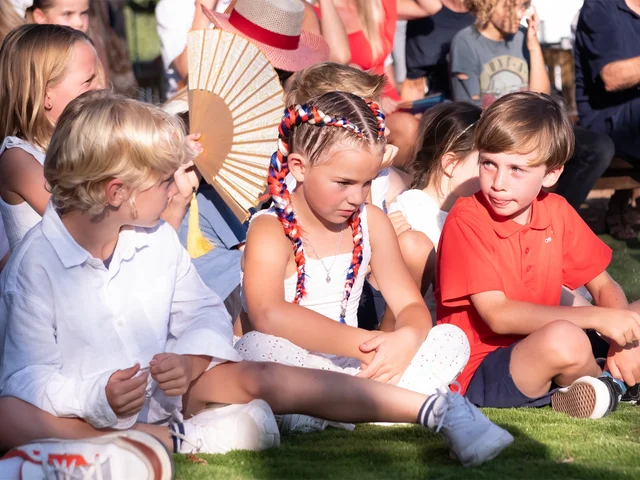 Young students in white sitting on the grass watching the performances