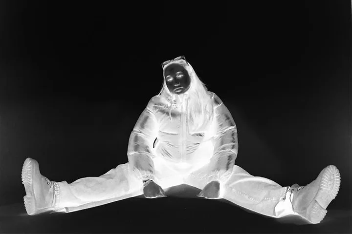 A figure in a white suit sitting against a black background