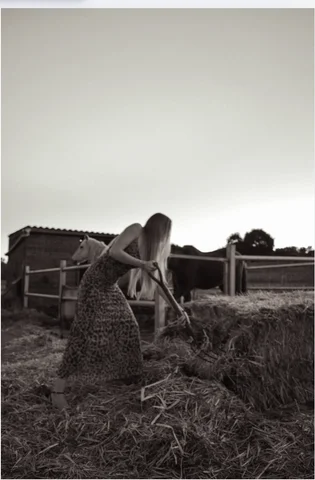 Sepia photograph of a woman raking hay by a farm