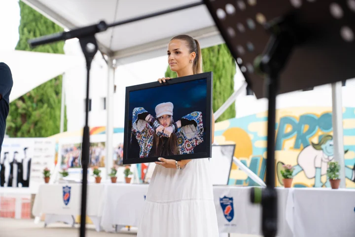 A student on stage holding up a framed portrait photograph for auction