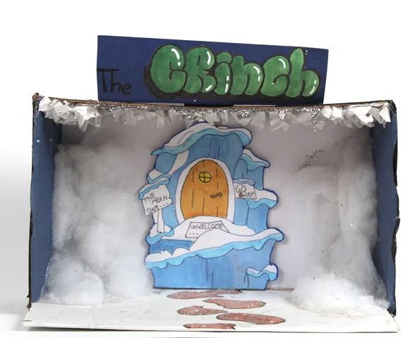 A Grinch-themed shoebox diorama with a snowy door