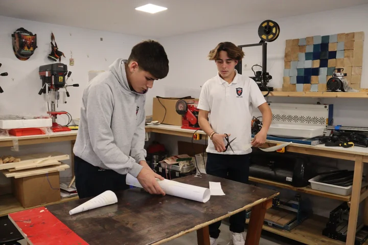 Two students working in the Design & Technology workshop with a pillar drill and 3D printer behind