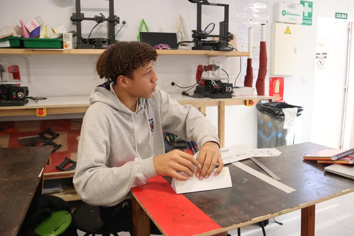 A student folding a paper structure at a workbench