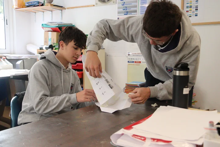 Two students taping a paper structure together