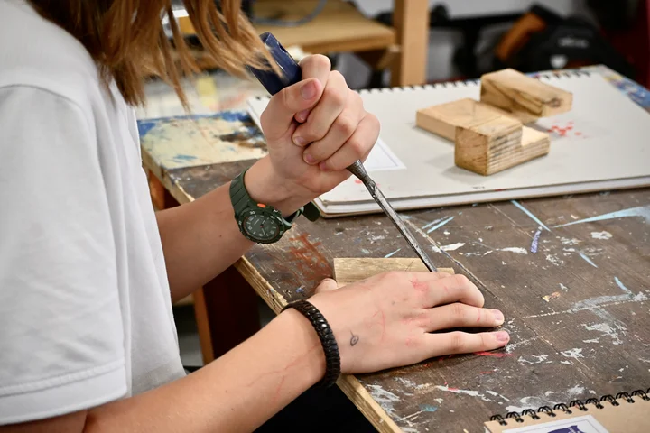 A student cutting into a block of wood with a chisel