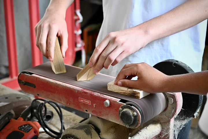 Students smoothing pieces of wood on the belt sander