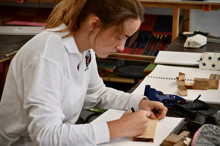 A student marking out her wooden piece beside her sketchbook