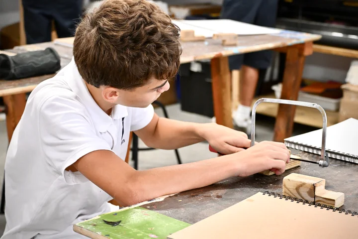 A student cutting a wooden block with a coping saw