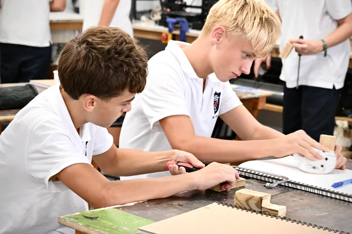 Two students working on their wooden pieces side by side