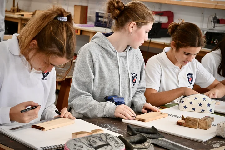 Three students measuring and marking out wood at the workbench