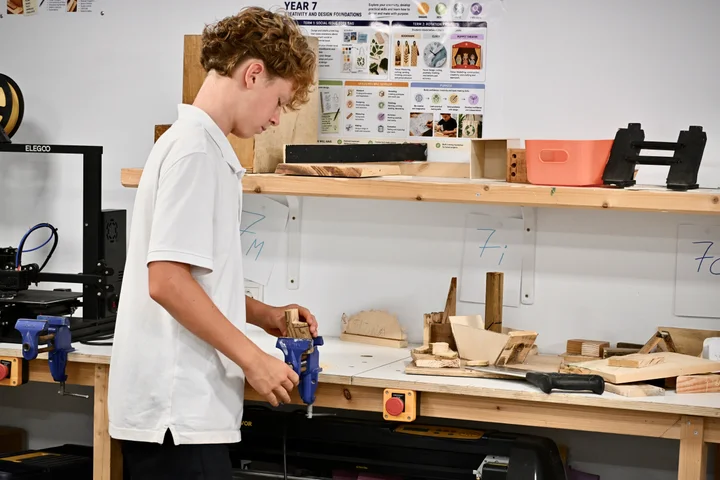 A student working at the bench vice in front of the Year 7 project display