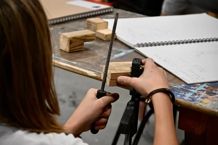 A student filing a wooden piece held in the vice