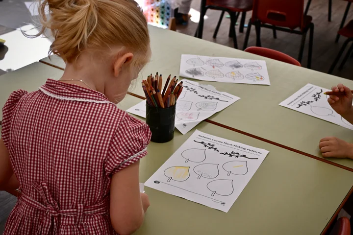Children working on autumn leaf mark-making sheets at a shared table
