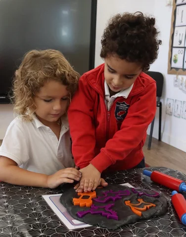 Two children pressing shapes into dough with rolling pins
