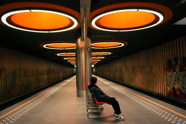 A figure waiting on a metro platform under orange lights