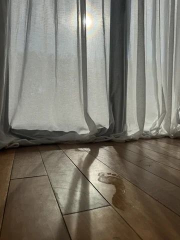 Wet footprints on a wooden floor beside sheer curtains