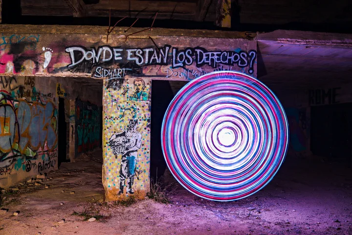 Light painting: a glowing pink and blue circle beside graffiti in an abandoned building at night