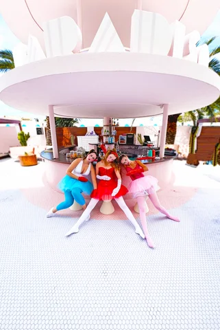 Three girls in bright dresses under a pink pavilion