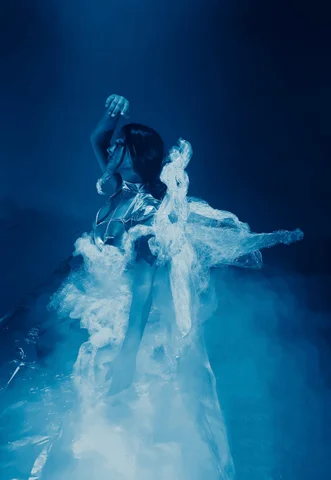A dancer surrounded by swirling smoke under blue light