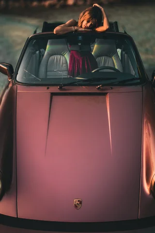 A girl leaning on the windscreen of a vintage Porsche