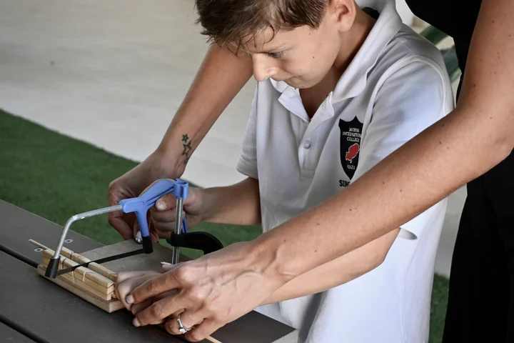 A pupil sawing a dowel held in a wooden bench hook
