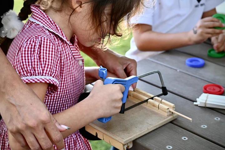 Close-up of a pupil using a hacksaw on a bench hook, with plastic wheels on the table