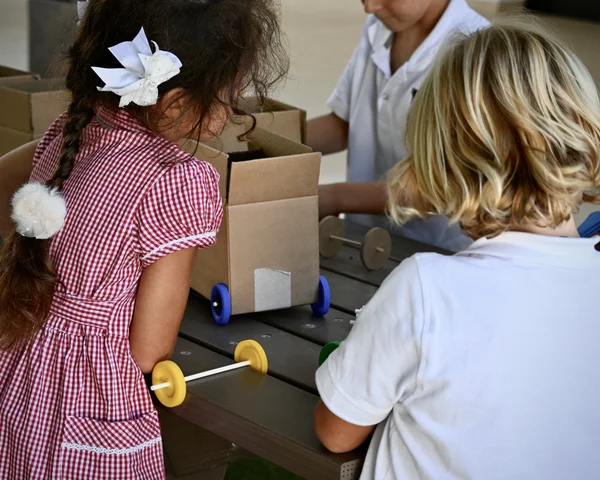 Pupils building cardboard vehicles with wooden axles and coloured wheels