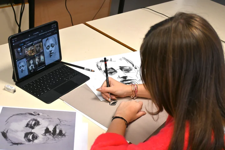 A student drawing a portrait from a reference on a tablet