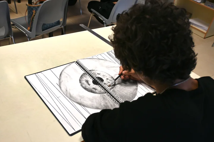 A student shading a detailed drawing of an eye in a sketchbook