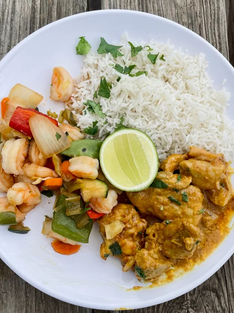 A lunch plate of rice, prawn stir-fry and curry with a wedge of lime