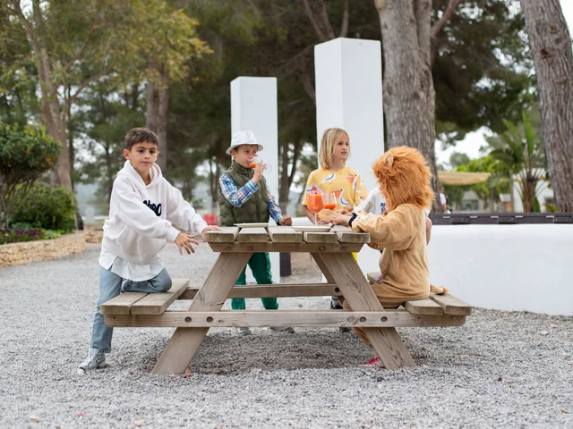 Primary children at a picnic bench with a classmate in a lion costume