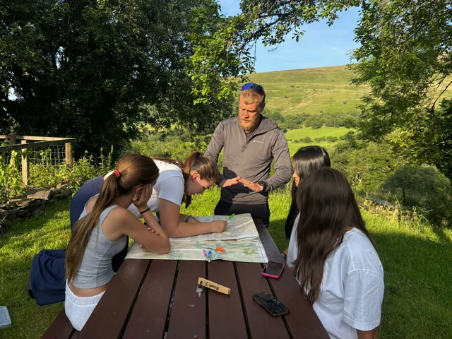Students planning their route on a map at a picnic table with their instructor