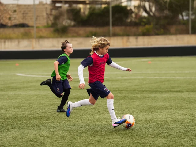 A young player in a red bib dribbling past a defender