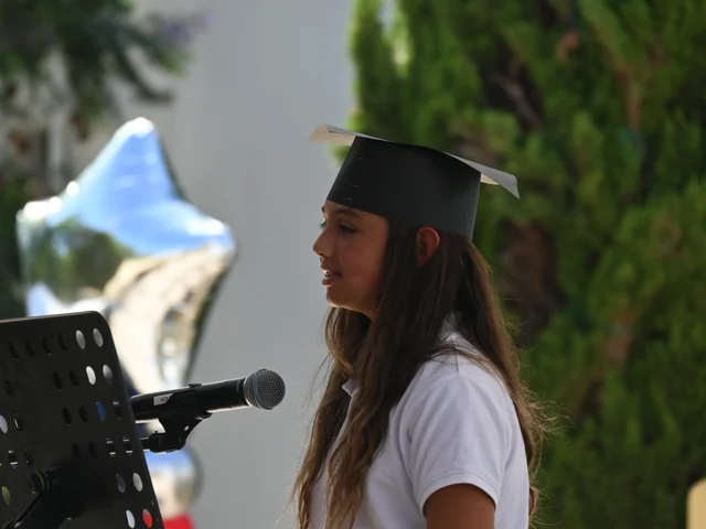 A pupil in a graduation cap speaking at the microphone
