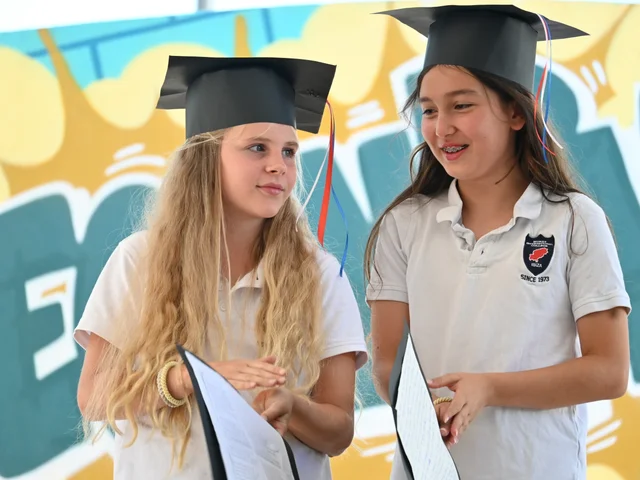 Two pupils in graduation caps holding their certificates
