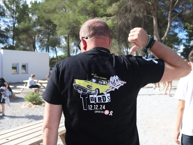 A teacher showing off the back of his black T-Birds charity T-shirt