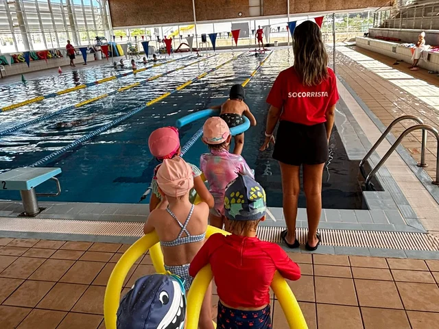 Young children with swimming noodles at the edge of the pool with their teacher