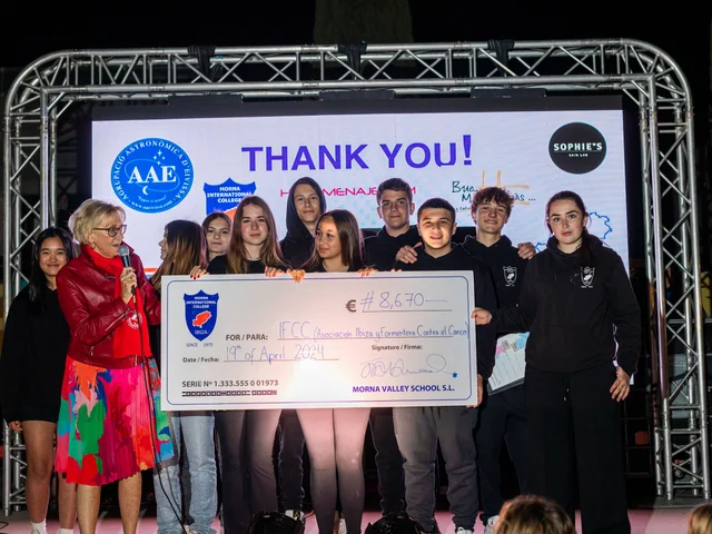 Students presenting the €8,670 cheque on stage with a thank-you screen