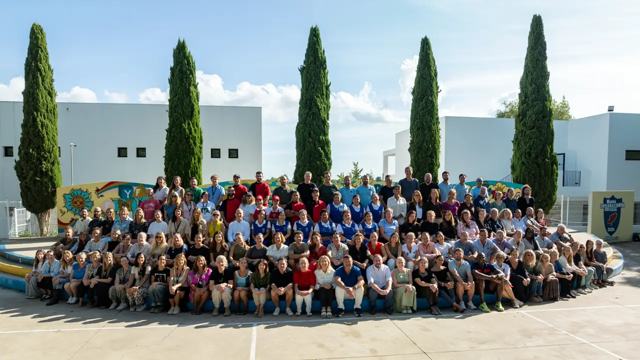 The whole Morna staff seated together on the curved playground steps, with cypress trees and the school buildings behind