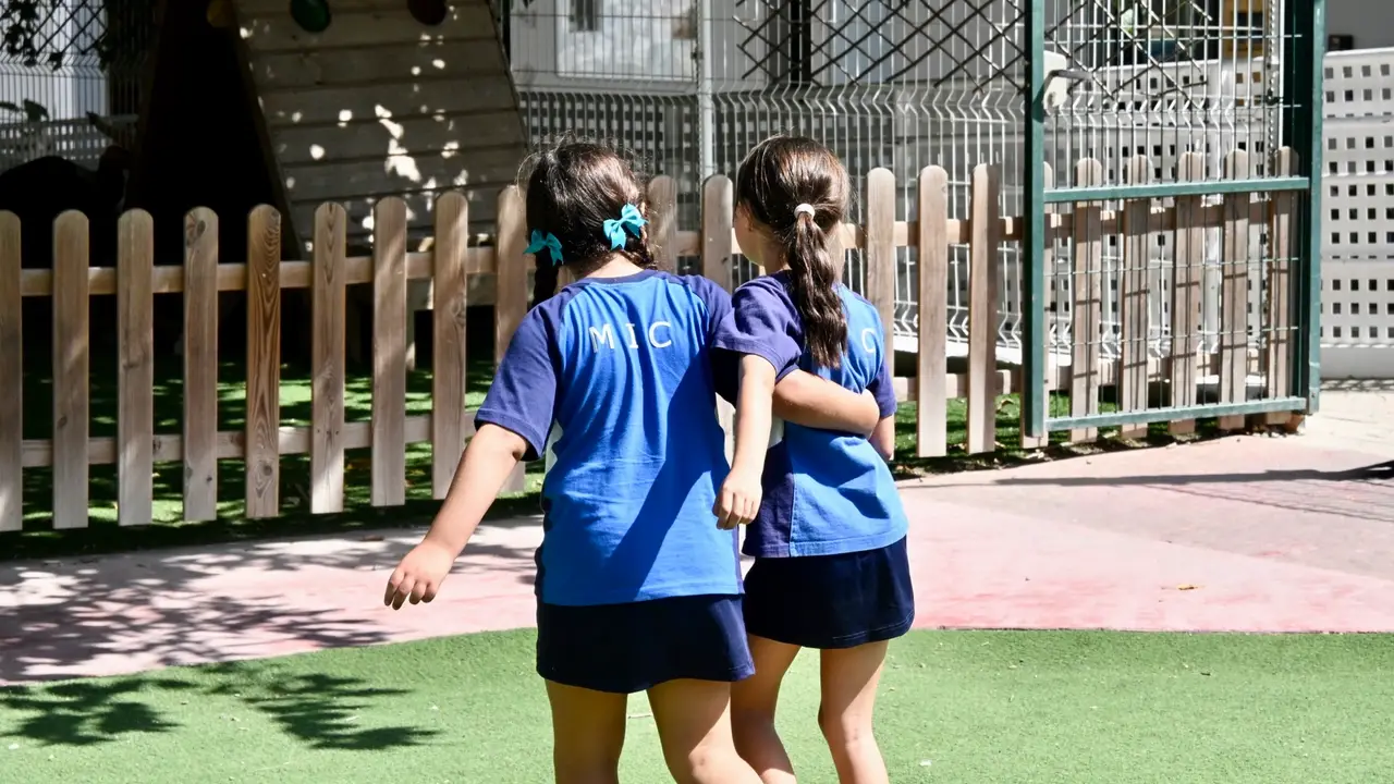 Two Primary pupils walking arm in arm across the playground